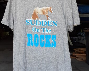 Puede incluir: Camiseta gris con un gráfico de un caballo marrón y texto azul que dice "Sudden On The Rocks".