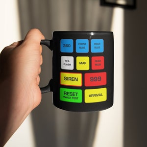 May include: Black ceramic mug featuring a control panel design with buttons labelled 360, Front Blue, Rear Blue, H/L Flash, Map, Rear Reds, Siren, 999, Reset Walk Test, and Arrival.