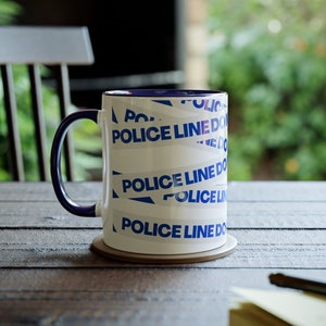 May include: White ceramic mug with a blue rim and blue and white "Police Line Do Not Cross" tape design.