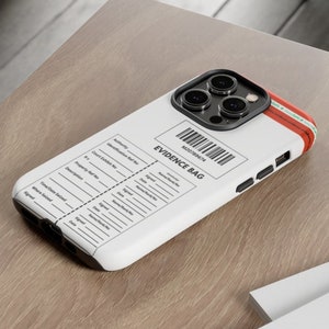 May include: White iPhone case with a red and black stripe. The case has a form for evidence collection with the text "Evidence Bag" and a barcode. The case is on a wooden surface.