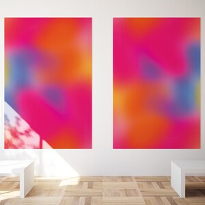 May include: Two abstract paintings with a blurred, colorful design. The paintings are in shades of pink, orange, blue, and purple. The paintings are hanging on a white wall in a gallery setting.