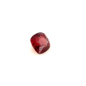 May include: A deep red gemstone with a cushion cut. The gemstone is set against a white background.