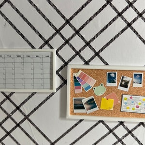 May include: A white framed corkboard with a variety of items pinned to it, including photos, a color palette, a frog sticker, and a small calendar with the word "Schedule" printed on it. There is also a white framed calendar with the days of the week labeled.