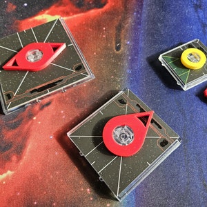 Könnte beinhalten: Drei verschiedene Spielsteine mit roten und gelben Akzenten. Die Steine befinden sich auf einem schwarzen und blauen Hintergrund.