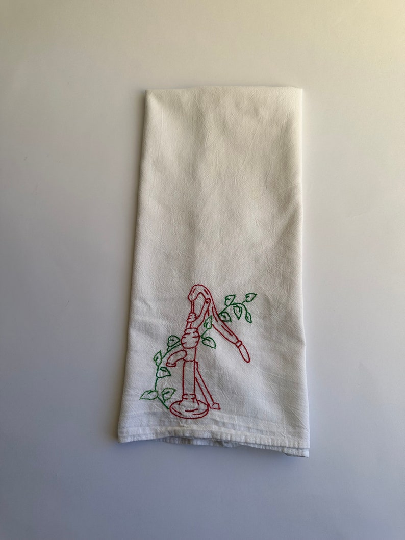 May include: White kitchen towel with red and green embroidery of a hand pump with vines.