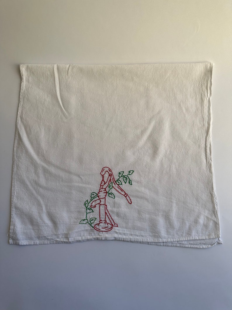 May include: White kitchen towel with red and green embroidery of a hand pump with vines.