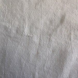 May include: White fabric with a textured, woven pattern. The fabric has a slightly wrinkled appearance.