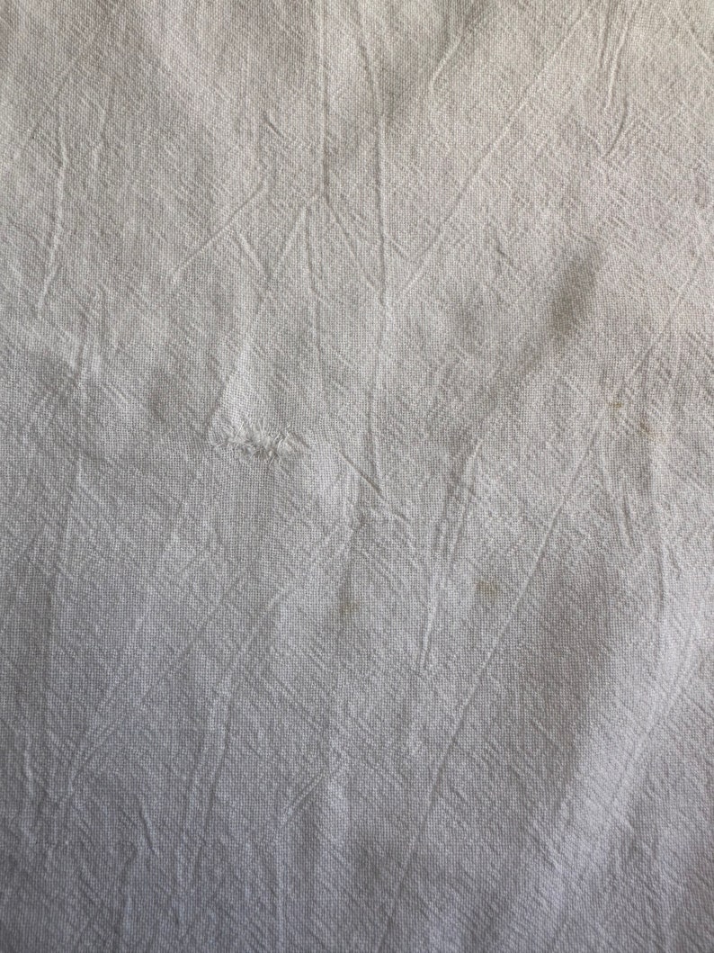 May include: White fabric with a textured, woven pattern. The fabric has a slightly wrinkled appearance.