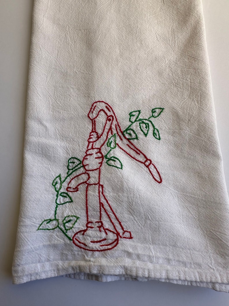May include: A white tea towel with red and green embroidery of a hand pump with vines.