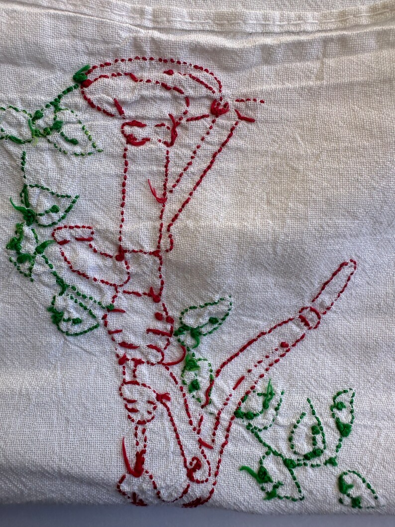 May include: White fabric with red and green embroidery of a flower with a stem and leaves.