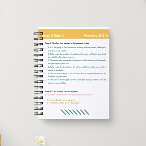 May include: A spiral-bound notebook with the text "Week 3 | Day 2" and "Proverbs 25:5-6" in yellow and white. The notebook contains numbered verses and a memory jogger exercise. A pencil and a bowl of popcorn are in the background.