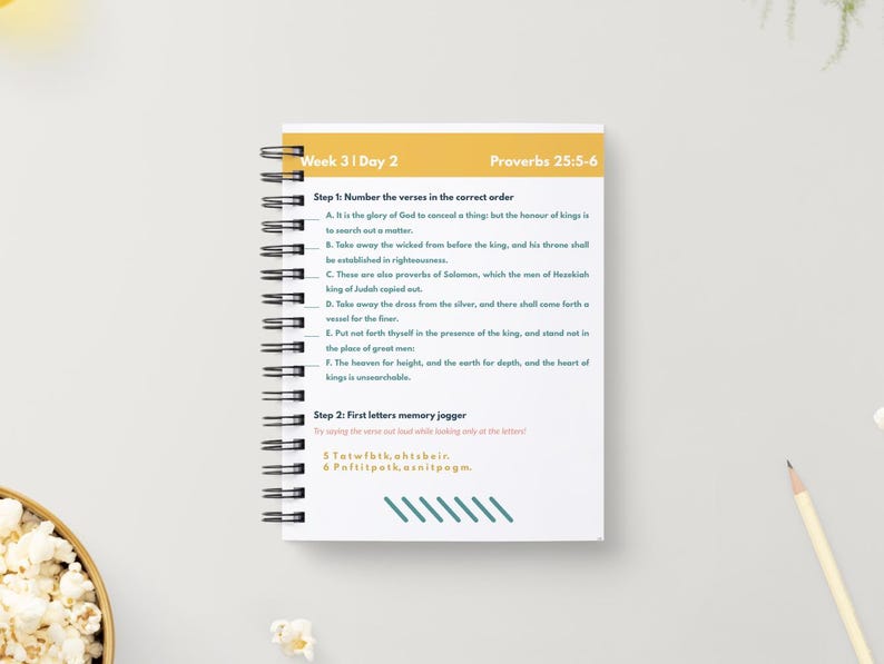 May include: A spiral-bound notebook with the text "Week 3 | Day 2" and "Proverbs 25:5-6" in yellow and white. The notebook contains numbered verses and a memory jogger exercise. A pencil and a bowl of popcorn are in the background.