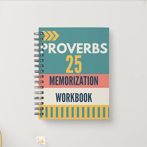 May include: A spiral-bound workbook with a teal cover featuring the text "PROVERBS 25 MEMORIZATION WORKBOOK." The text is in white and yellow, with a coral and cream stripe design. The notebook is on a white surface.