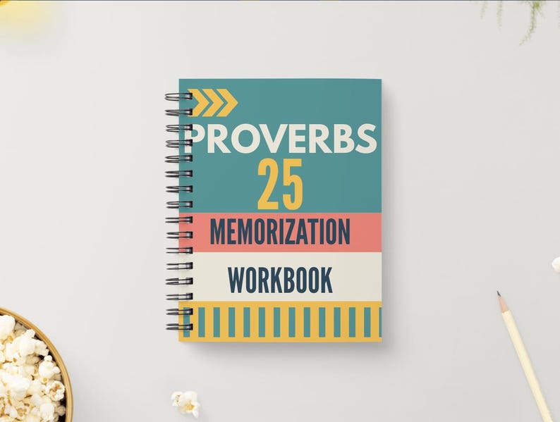May include: A spiral-bound workbook with a teal cover featuring the text "PROVERBS 25 MEMORIZATION WORKBOOK." The text is in white and yellow, with a coral and cream stripe design. The notebook is on a white surface.