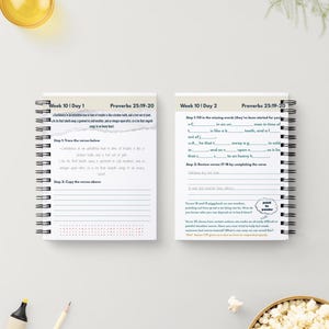 May include: Two spiral-bound notebooks with white pages, featuring text and prompts for Week 10, Day 1 and Day 2, with the text "Proverbs 25:19-20". The notebooks are on a white surface, with a yellow liquid in a glass and a bowl of popcorn in the background.