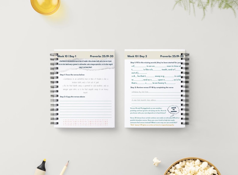 May include: Two spiral-bound notebooks with white pages, featuring text and prompts for Week 10, Day 1 and Day 2, with the text "Proverbs 25:19-20". The notebooks are on a white surface, with a yellow liquid in a glass and a bowl of popcorn in the background.