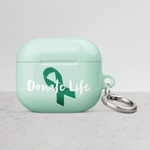 May include: A light green Airpods case with a green ribbon and the text "Donate Life" printed on the front. The case has a silver keychain attached.