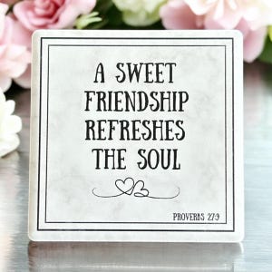 Puede incluir: Un letrero cuadrado blanco con texto negro que dice "Una dulce amistad refresca el alma" con dos corazones y el texto "Proverbios 27:9" en la parte inferior.