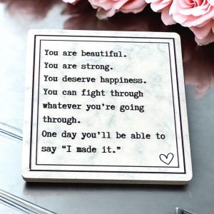 Può includere: Un sottobicchiere in marmo bianco con testo nero che recita "You are beautiful. You are strong. You deserve happiness. You can fight through whatever you're going through. One day you'll be able to say "I made it."  Un piccolo simbolo di cuore si trova nell'angolo in basso a destra.
