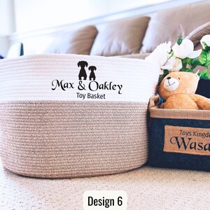 May include: White and beige rope storage basket with the text "Max & Oakley Toy Basket" and two dog silhouettes. The basket is sitting on a white carpet with a small black and brown storage basket in the background.