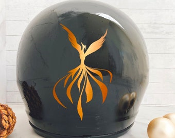 May include: A black motorcycle helmet with a gold phoenix decal. The helmet is sitting on a white surface.