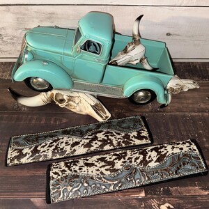 May include: A turquoise vintage toy truck with a skull in the bed and two cowhide patterned wallets. The wallets have a brown and white spotted pattern with a blue floral design.