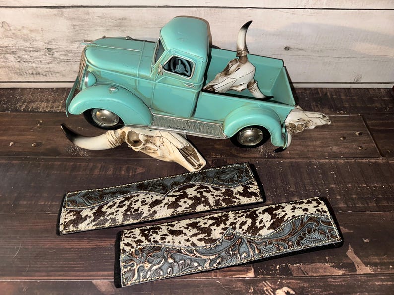 May include: A turquoise vintage toy truck with a skull in the bed and two cowhide patterned wallets. The wallets have a brown and white spotted pattern with a blue floral design.