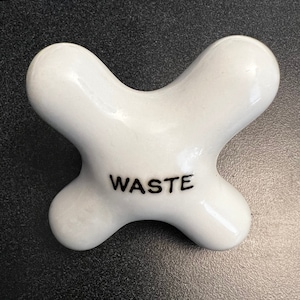 May include: White ceramic waste bin with the word "WASTE" printed in black lettering.