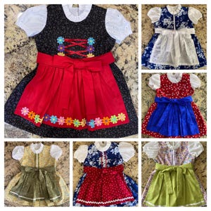 Pode incluir: Uma cole&ccedil;&atilde;o de vestidos dirndl coloridos. Os vestidos apresentam uma variedade de padr&otilde;es, incluindo florais e bolinhas, com detalhes como flores bordadas, la&ccedil;os e rendas. A paleta de cores inclui vermelho, azul, verde e amarelo.
