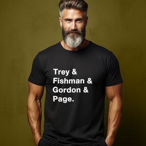 以下が含まれることがあります： 白文字で「Trey & Fishman & Gordon & Page」と書かれた黒いTシャツ。クルーネックのスタイルです。背景はオリーブグリーンの無地です。
