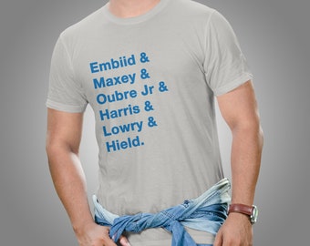 May include: A white t-shirt with blue text that reads "Embiid & Maxey & Oubre Jr & Harris & Lowry & Hield."