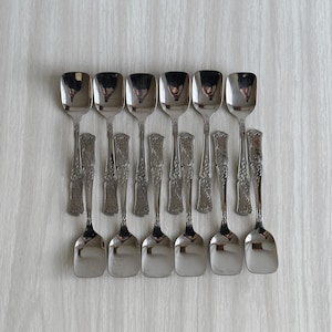 Puede incluir: Conjunto de diez cucharas de helado cuadradas adornadas, de color plateado.