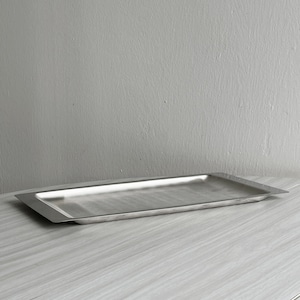 Könnte beinhalten: Ein rechteckiges Serviertablett aus Edelstahl mit leicht erhöhtem Rand. Das Tablett ist silberfarben und steht auf einer hellen Holzoberfläche. Das Tablett ist leer und einsatzbereit.