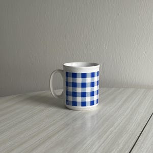 Pode incluir: Uma caneca de cerâmica branca com um padrão xadrez azul e branco.