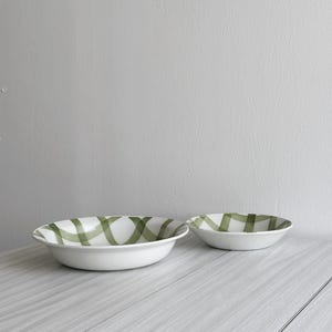 以下が含まれることがあります： 緑と白の市松模様の白いセラミックボウルが2つ。大きなボウルは手前に、小さなボウルは奥にあります。
