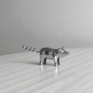 Peut inclure: Un tire-bouchon en forme de cochon de couleur argentée. Le cochon a une surface brillante et réfléchissante et une queue en tire-bouchon. L'outil est conçu pour retirer les bouchons des bouteilles de vin. Le cochon est sur une surface claire.