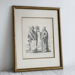 Peut inclure: Une estampe encadrée en noir et blanc d'une gravure historique représentant deux personnages, un homme et une femme, debout côte à côte. L'homme tient une lance et un bouclier, tandis que la femme tient une petite maquette de bâtiment. Le texte "BALDWINVS QVINTVS IMPERATOR" est imprimé sous les personnages.