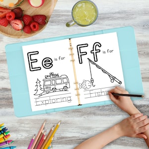 Puede incluir: Un libro para colorear abierto en las letras E y F. La letra E es para Explorar, con un dibujo de un autobús. La letra F es para Pescar, con un dibujo de un pez y una caña de pescar. Una mano sostiene un lápiz.