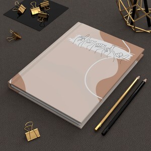 May include: A beige journal with a white and brown abstract design. The journal has a line drawing of hands signing the word "love".