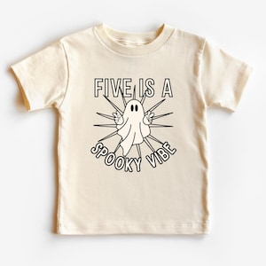 以下が含まれることがあります： クリーム色の半袖Tシャツに、黒と白の幽霊のグラフィックと「FIVE IS A SPOOKY VIBE」のテキストがプリントされています