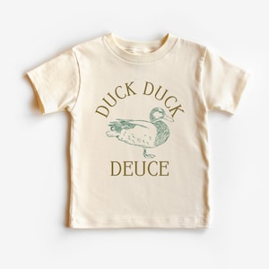 May include: Cream-colored toddler t-shirt with a green duck illustration and the words "DUCK DUCK DEUCE" printed on the front. The design features a sketch-style drawing of a duck. The shirt has short sleeves and a crew neck.