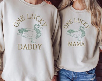 May include: Two cream-colored sweatshirts with a green duck illustration and the text "One Lucky Daddy" and "One Lucky Mama".