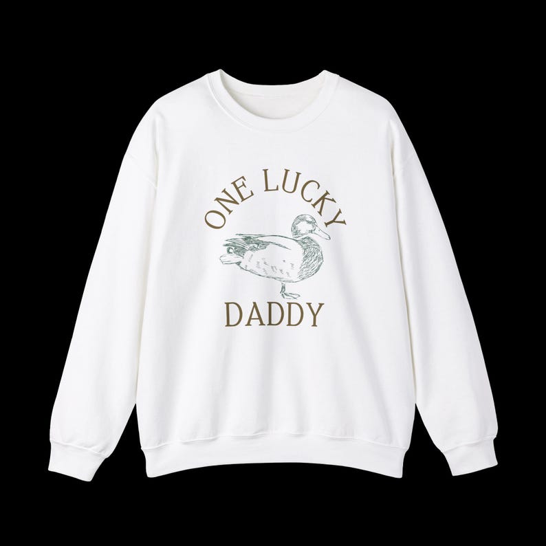 以下が含まれることがあります： 白地に緑色のアヒルのイラストと、茶色の文字で「One Lucky Daddy」と書かれたスウェットシャツです。