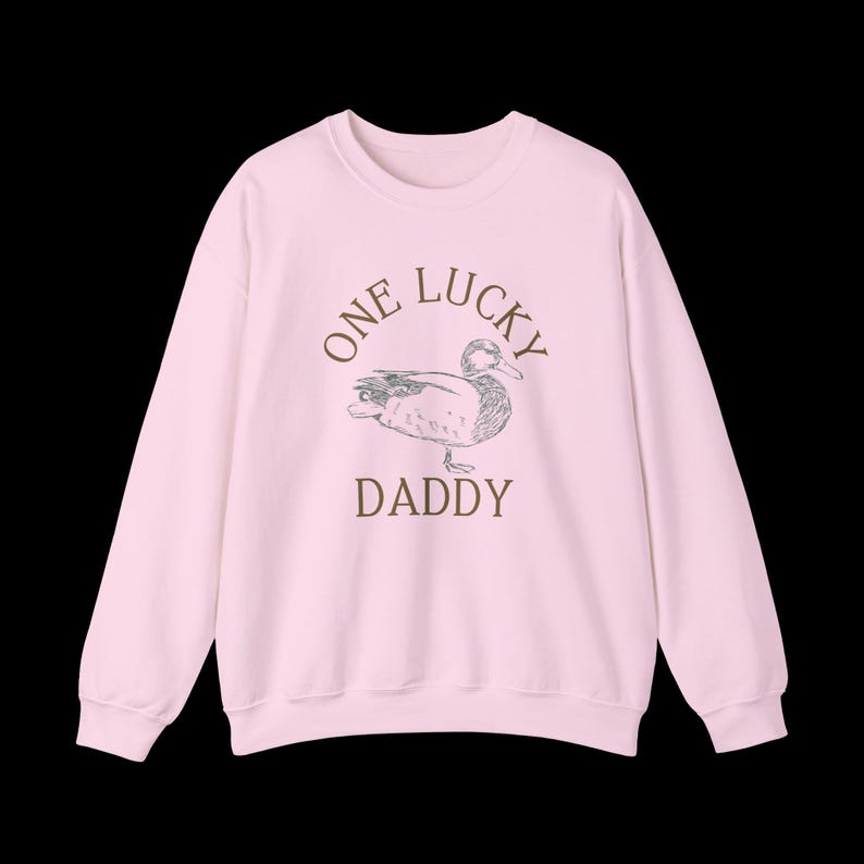 以下が含まれることがあります： 「One Lucky Daddy」という文字とアヒルの絵が描かれたピンク色のスウェットシャツです。