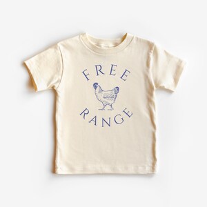May include: Cream-colored short-sleeved t-shirt with the words "FREE RANGE" in navy blue arched above and below a navy blue illustration of a chicken. The shirt is made of soft material.
