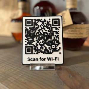 May include: White sign with a black QR code and the text "Scan for Wi-Fi". The sign is on a wooden surface with two bottles of liquor in the background.