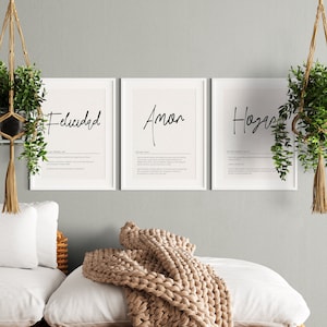 Puede incluir: Tres impresiones enmarcadas blancas con caligrafía negra sobre un fondo blanco. Las impresiones presentan las palabras en español "Felicidad", "Amor" y "Hogar" con definiciones debajo de cada palabra.