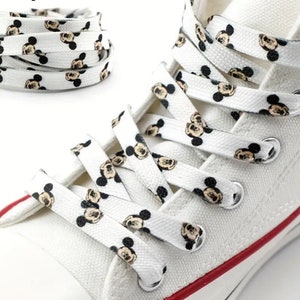 Op de afbeelding: Witte canvas schoenen met rode bies en zwart-witte Mickey Mouse-schoenveters.