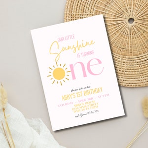K&ouml;nnte beinhalten: Eine wei&szlig;e Einladungskarte mit einem pinkfarbenen und gelben Sonnenmotiv. Der Text lautet "Our Little Sunshine is Turning One" und enth&auml;lt Details zur 1. Geburtstagsfeier von Abby.