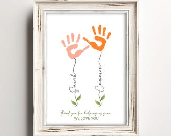May include: A white frame with a white background and two handprints in orange and pink. The handprints are connected by stems with leaves and the names "Sarah" and "Cameron" written vertically. The text "Thank you for helping us grow. We love you" is at the bottom of the frame.